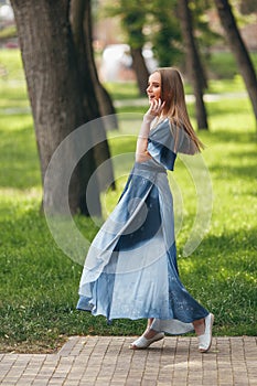 Stylish girl posing in a dress in a sunny spring park. Cheerful, happy portrait of a beautiful girl in the summer