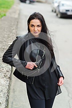 Stylish girl posing in street in fashionable outfit. Woman in black leather jacket and small leather fanny pack