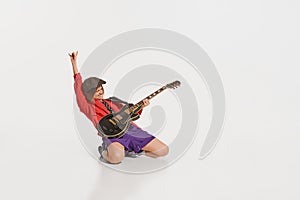 Stylish girl, retro musician wearing vintage style bright clothes playing guitar like rockstar  on white