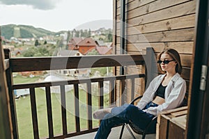 Stylish girl sitting in armchair on balcony with beautiful view, vacation at country house concept. Relax at the cottage, stylish