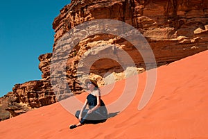 Stylish girl sitting on red dune relaxing and enjoying vacation retreat. Inspiration, travel mental health concept