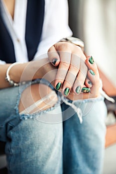 Stylish girl sitting in torn jeans and modern green nail Polish, watch, bracelet. Fashion, lifestyle, beauty, clothing.