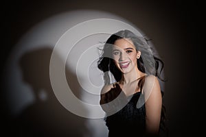 Stylish girl smiling at the camera. Curly hair dissipates. Confident look. Bright makeup. Game with studio light. Shadow