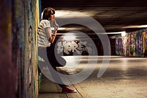 Stylish girl standing in grunge graffiti tunnel, shanty town