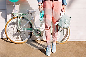 Stylish girl in trendy pink pants and sneakers standing on tiptoe holding backpack and headphones. Slim woman wearing
