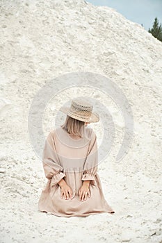 Stylish girl in trendy summer linen dress straw hat posing on the sand. Boho style.