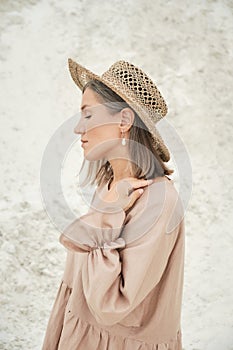 Stylish girl in trendy summer linen dress straw hat posing on the sand. Boho style.