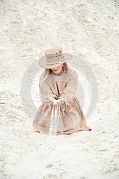 Stylish girl in trendy summer linen dress straw hat posing on the sand. Boho style.