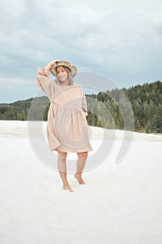Stylish girl in trendy summer linen dress straw hat posing on the sand. Boho style.