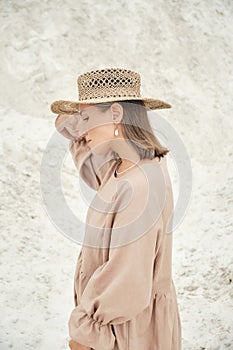 Stylish girl in trendy summer linen dress straw hat posing on the sand. Boho style.