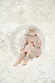 Stylish girl in trendy summer linen dress straw hat posing on the sand. Boho style.