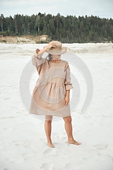 Stylish girl in trendy summer linen dress straw hat posing on the sand. Boho style.