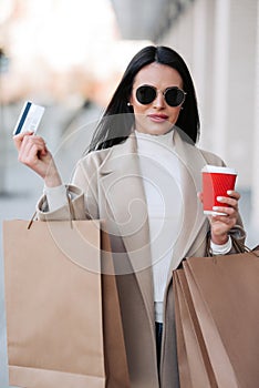 Stylish girl walking with coffee and shopping bags and doing shopping