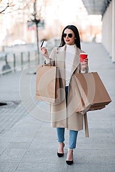 Stylish girl walking with coffee and shopping bags and doing shopping
