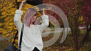 Stylish girl walks in colourful autumn park, puts on hat and smiles