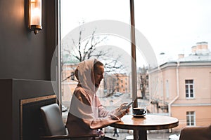 Stylish girl wear pink hoodie drinking coffee and typing message on phone in cafe