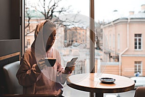 Stylish girl wear pink hoodie drinking coffee and typing message on phone in cafe.