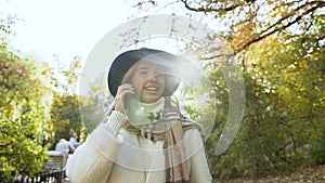 Stylish girl in the white coat speaking with someone on the mobile phone in the green park.