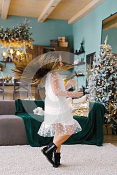 Stylish girl in a white dress whirls on the background of a Christmas tree in the living room in the house