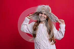 Stylish girl in winter earflap hat. Teen child wearing warm winter earflap hat. Girl kid isolated on red. Happy