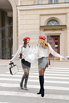 Stylish girlfriends with red berets in the style of French women smile and laugh, walking around the city, with shopping bags