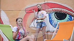 Stylish Girlfriends showing trick with spinners on background of graffiti, adolescents spin of toy for stress relief on