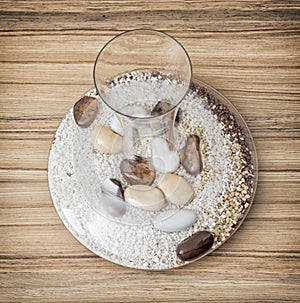 Stylish glass vase full of decorative stones on the wooden background