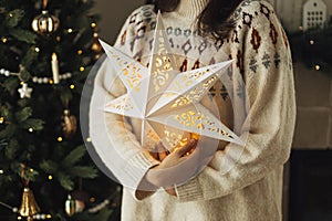 Stylish glowing big christmas star in hands of on background of decorated christmas tree with vintage baubles and lights. Merry