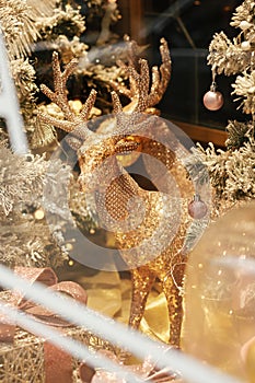 Stylish golden reindeer and modern christmas tree with glitter baubles in window, fairytale decoration. Atmospheric magic time.