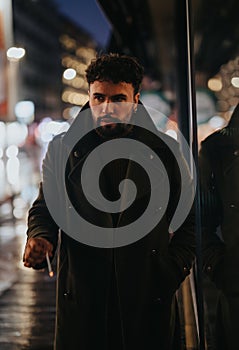 A stylish and good looking businessman waiting for a taxi on a rainy night in the busy downtown area of the urban city.