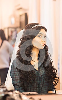 Stylish gorgeous bride getting makeup in the luxury beauty saloon with big mirrors and light.