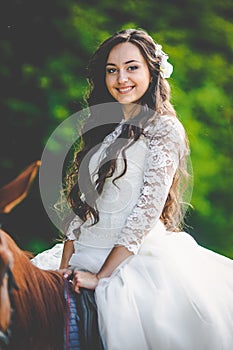 Stylish gorgeous happy brunette bride riding a horse on the back