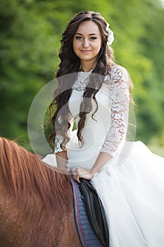 Stylish gorgeous happy brunette bride riding a horse on the back