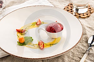 Stylish gourmet dessert with strawberry ice cream and fruit served on white plate at restaurant