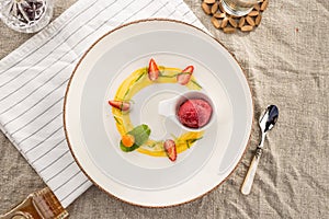 Stylish gourmet dessert with strawberry ice cream and fruit served on white plate at restaurant