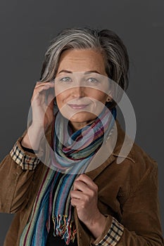 Stylish graying Woman charmingly smiles looking at camera. Caucasian mid aged beauty dressed in brown corduroy jacket