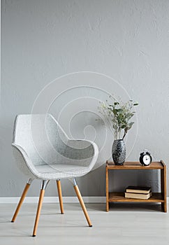 Stylish grey chair next to cabinet with vase and flowers in modern office interior, real photo