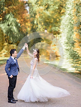 Stylish groom in blue jacket whirls happy bride in autumn park