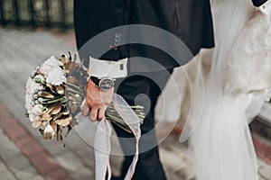 Stylish groom holding amazing bouquet of roses and golden leaves