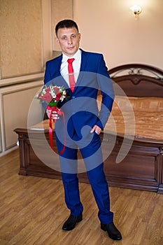 Stylish groom holds wedding bouquet. Young groom in a suit. Groom in classic clothes with bow tie