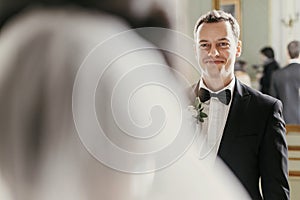 Stylish groom looking at his gorgeous bride in stylish dress with amazing bouquet posing in luxury room in hotel. beautiful woman