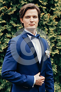 Stylish groom portrait in park. handsome man in blue suit posing in spring park. gentleman or businessman at reception outdoors