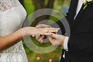 Stylish groom puts on the engagement ring on the finger of his beautiful bride at the wedding ceremony. Strong male