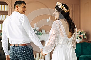 Stylish groom in a suit and a young bride in a wedding lace dress with a bouquet of flowers, sit together, hug, in the studio on