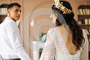 Stylish groom in a suit and a young bride in a wedding lace dress with a bouquet of flowers, sit together, hug, in the studio on