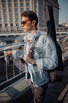 Stylish guy in denim jacket with a guitar in the city