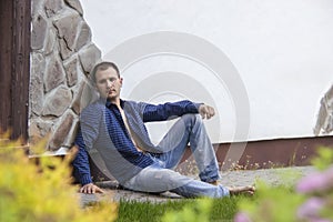 Stylish guy in shirt sits on floor while wall background and relaxes