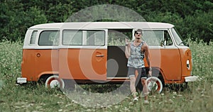 Stylish guy with sunglasses dancing amazing in front of retro van in the middle of nature