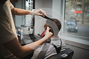 A stylish hairstylist serving client on a barbershop background. Hairdresser`s hands shaving male client`s head. Beauty