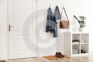 Stylish hallway interior with door, comfortable furniture and clothes on wall